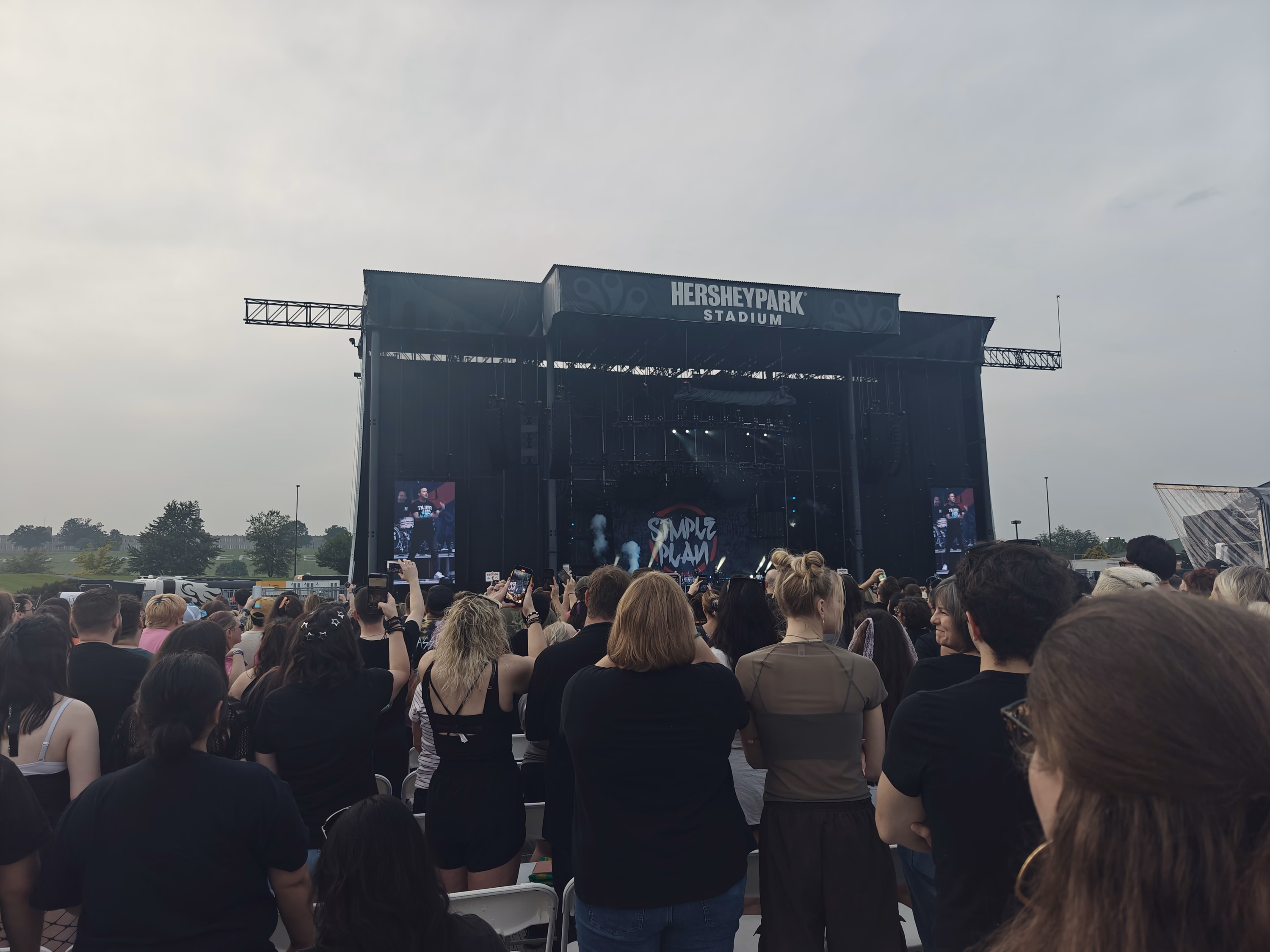 A dense crowd faces the full Hersheypark Stadium stage beneath a pale evening sky.