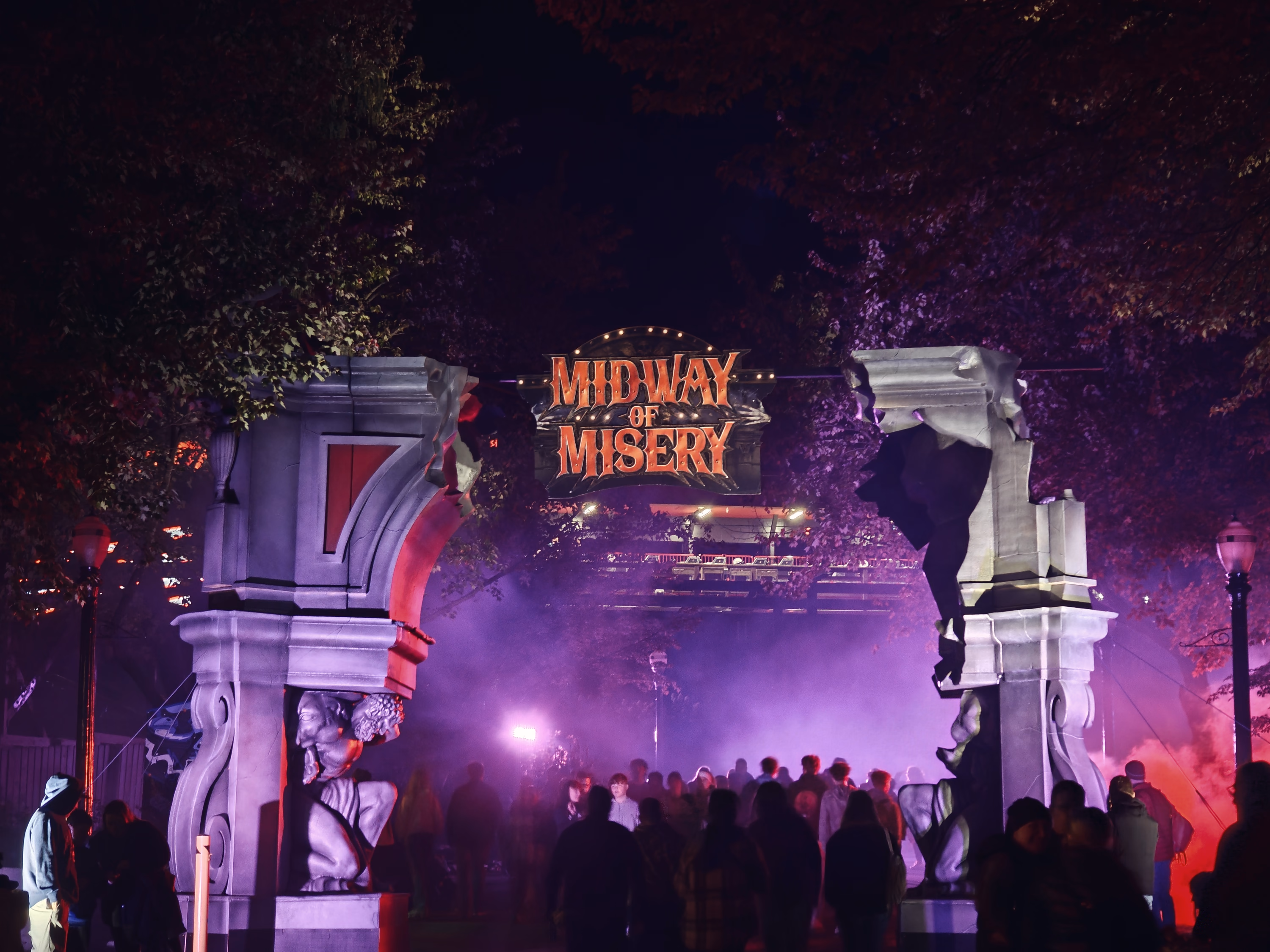 A broken-stone arch marked Midway of Misery opens onto purple fog and a crowd beneath dark trees.