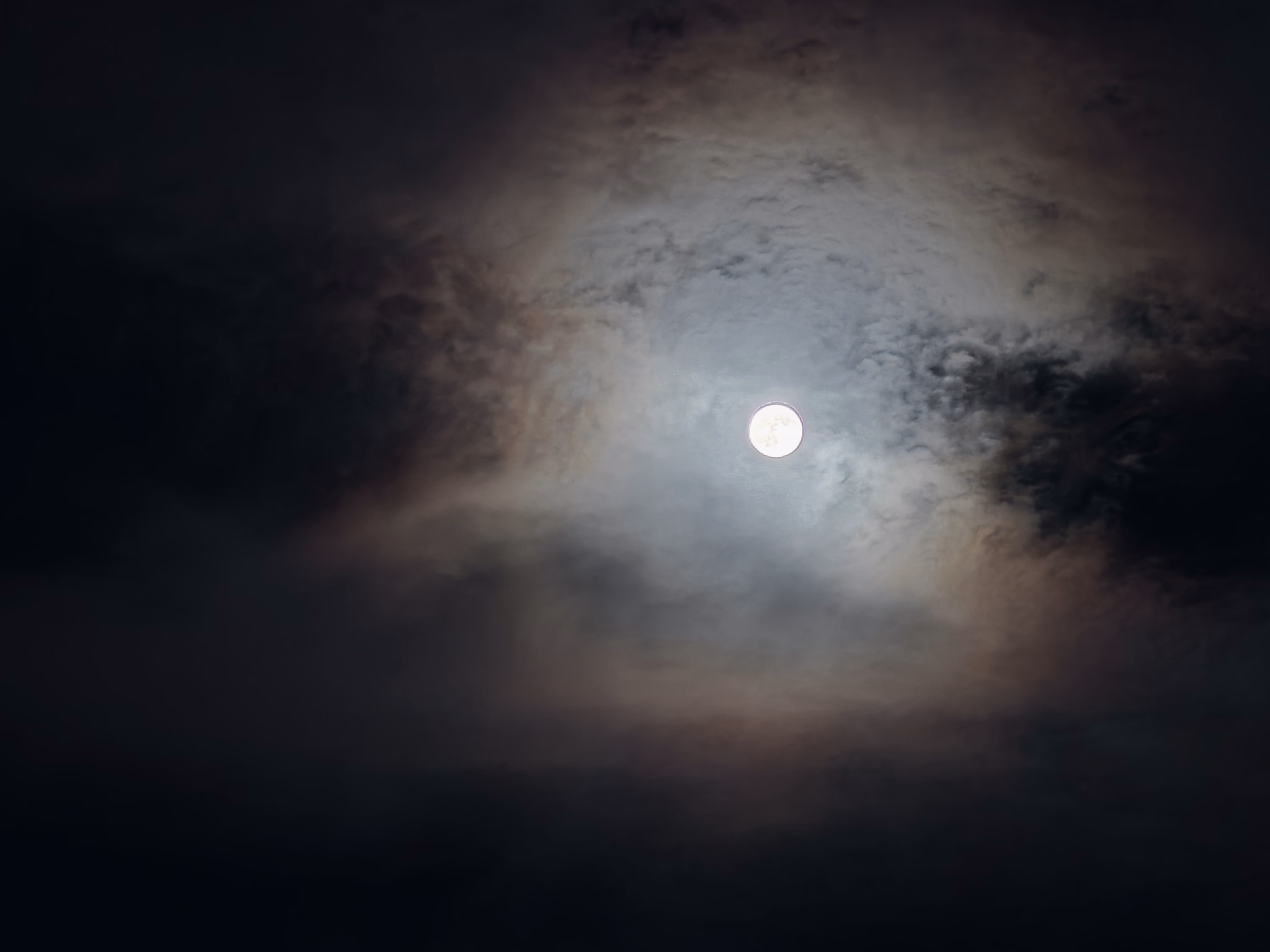A bright full moon sits inside a blue-gray opening surrounded by rust-colored cloud and black sky.
