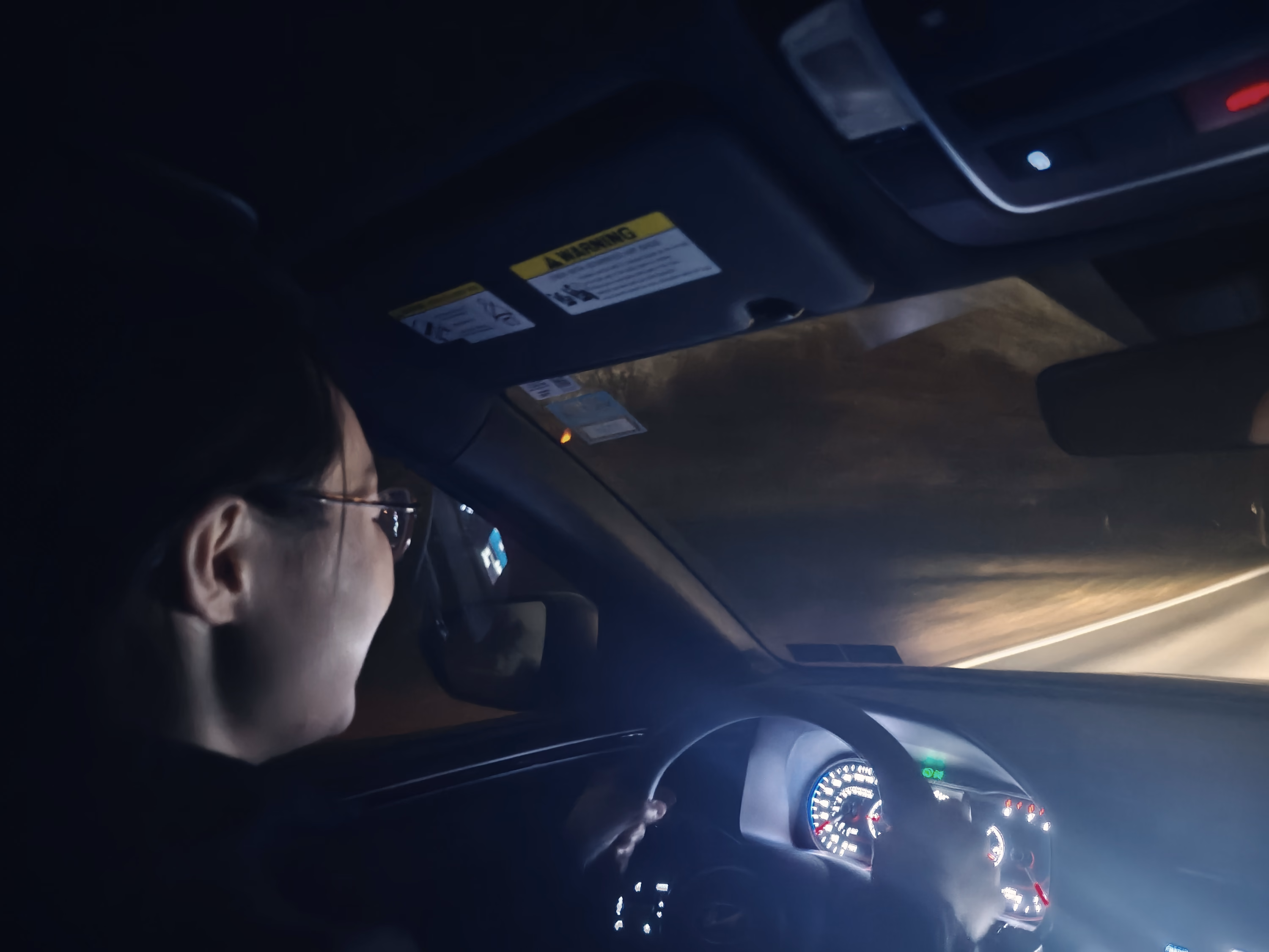 A driver in profile passes through blue dashboard light while the road becomes a warm streak beyond the windshield.