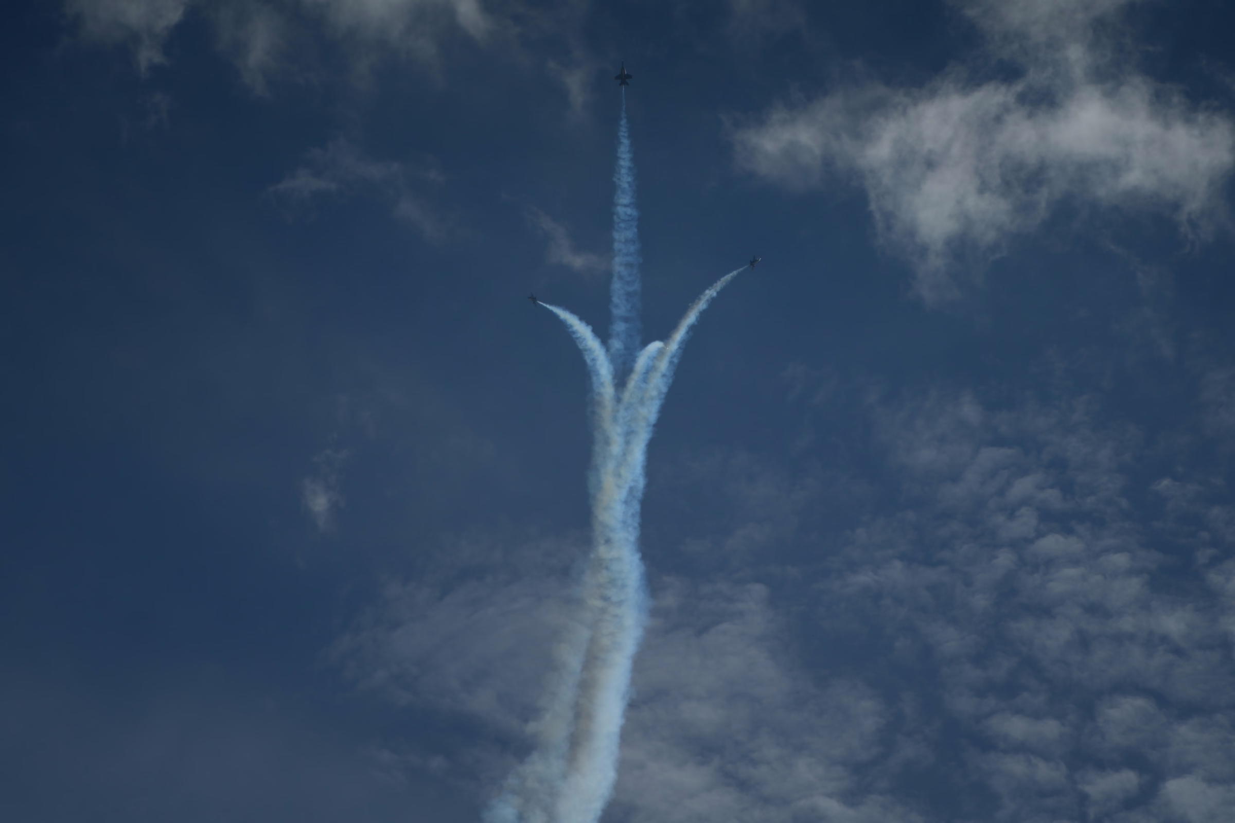 Three jets split from a rising column of white smoke, drawing a branching shape through a deep blue sky.