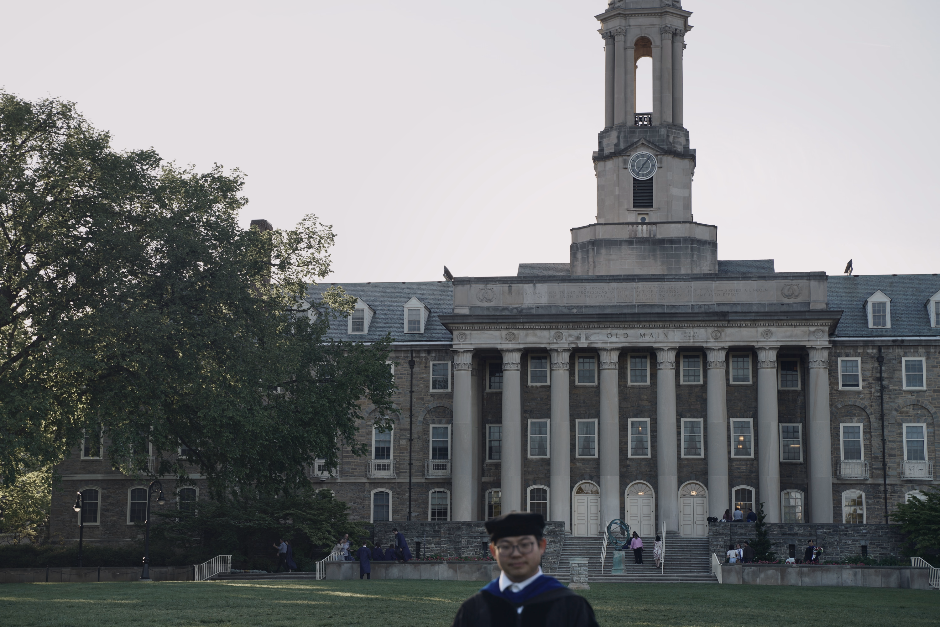 Wide view of Penn State Old Main with a graduate close to the camera at the lower edge.