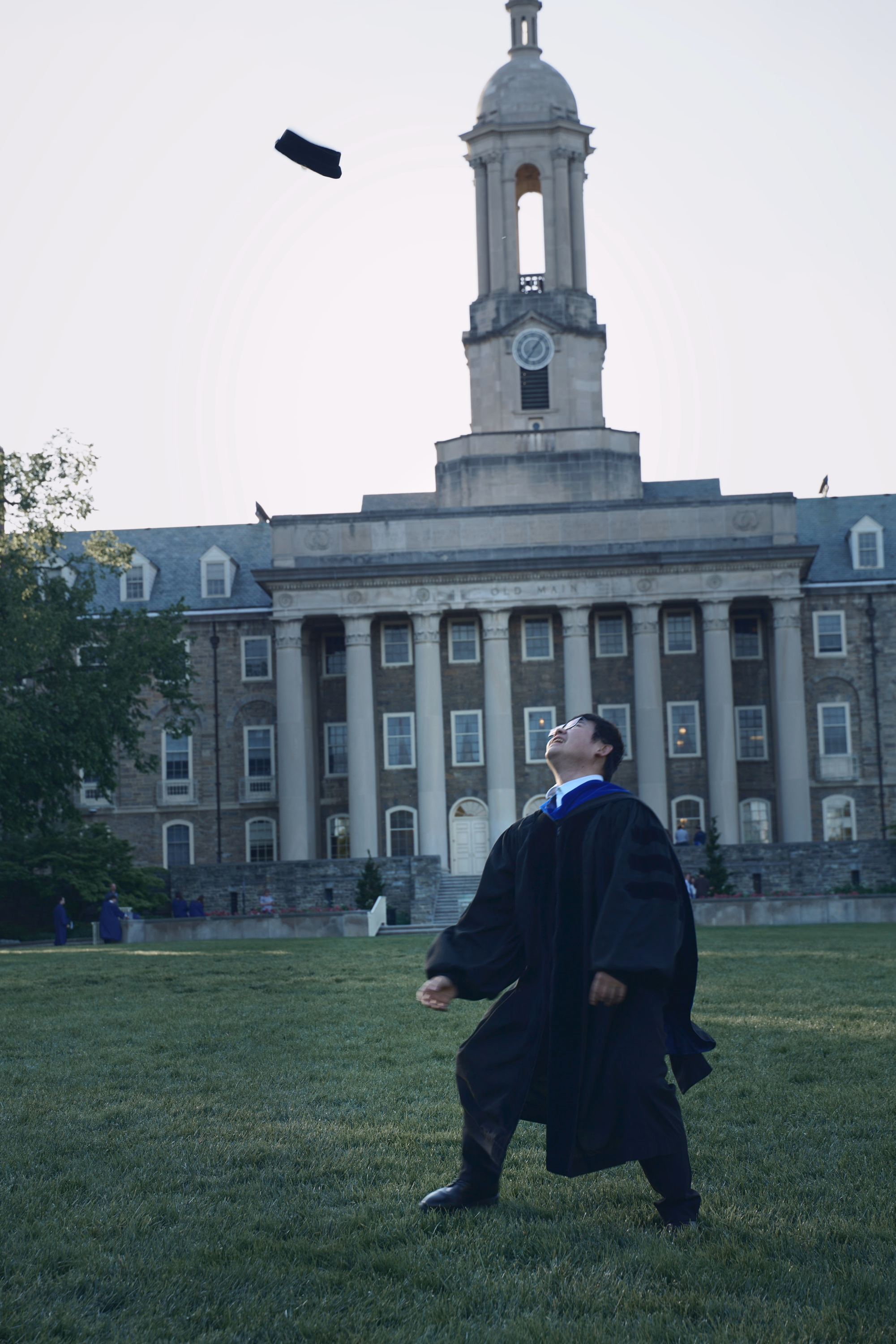 Graduate looking up at a falling mortarboard with Old Main directly behind.