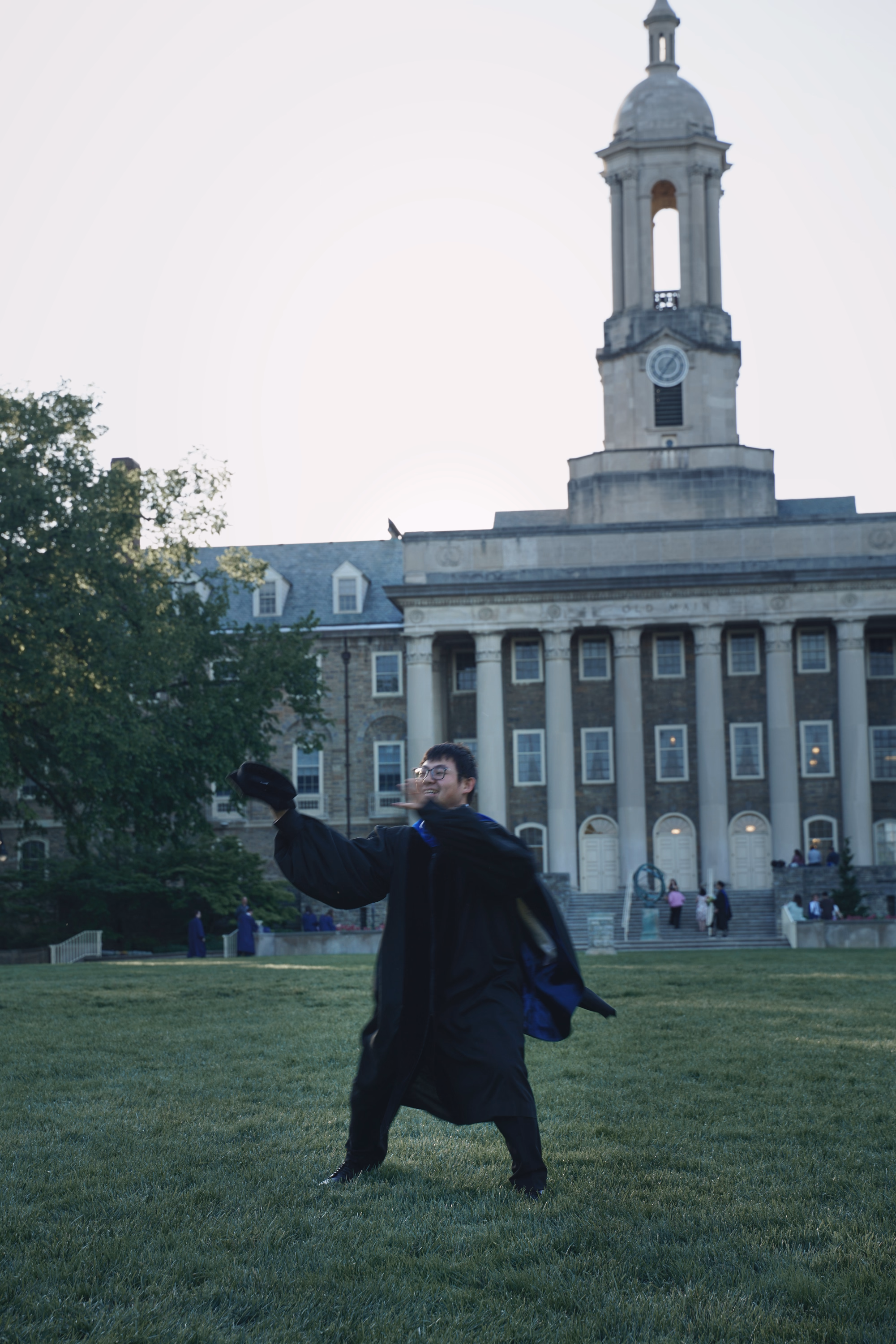 Graduate standing in a broad victory pose on the Old Main lawn.