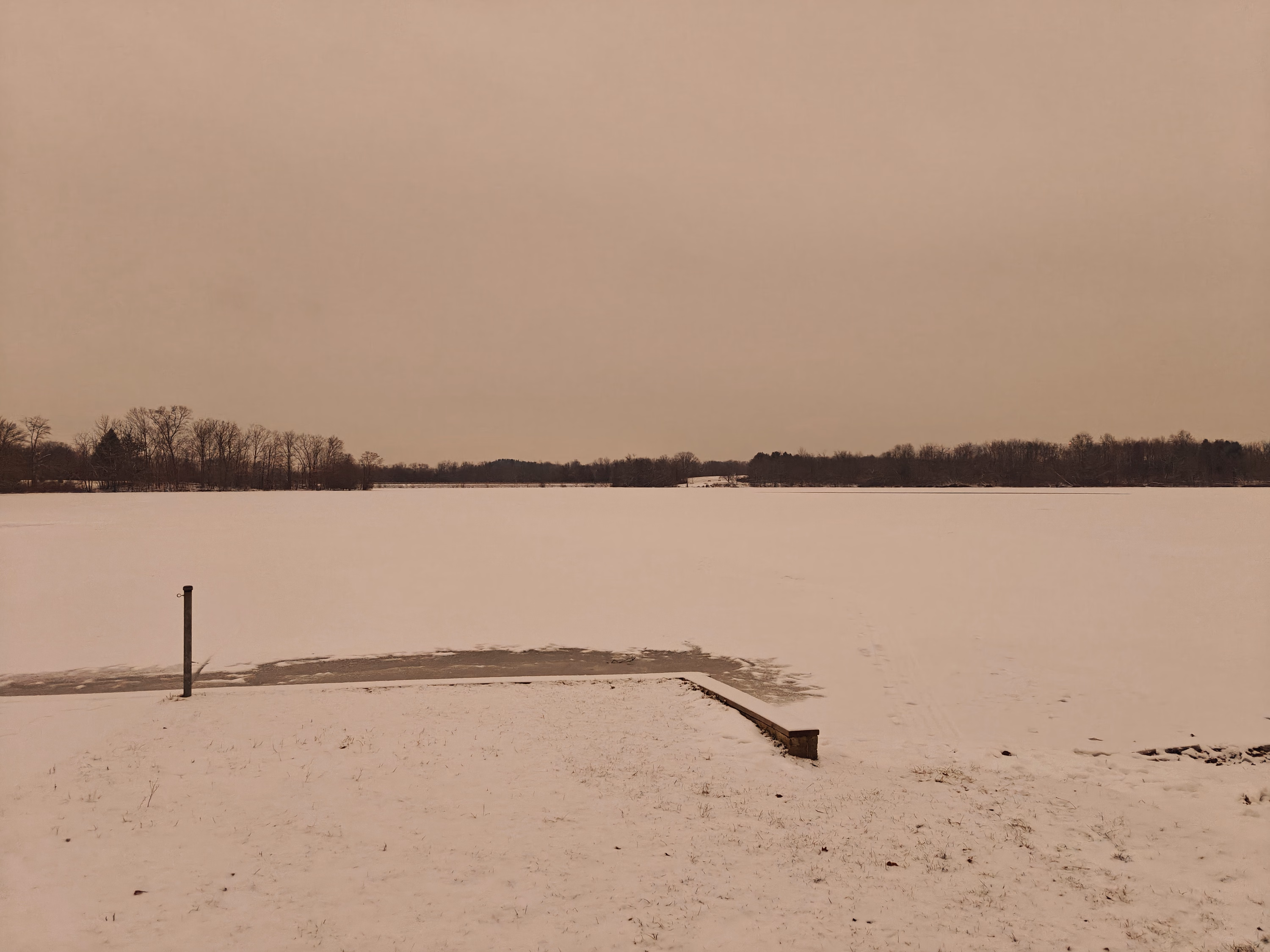 A small dock projects from a snowy field beside still water near Palmyra.