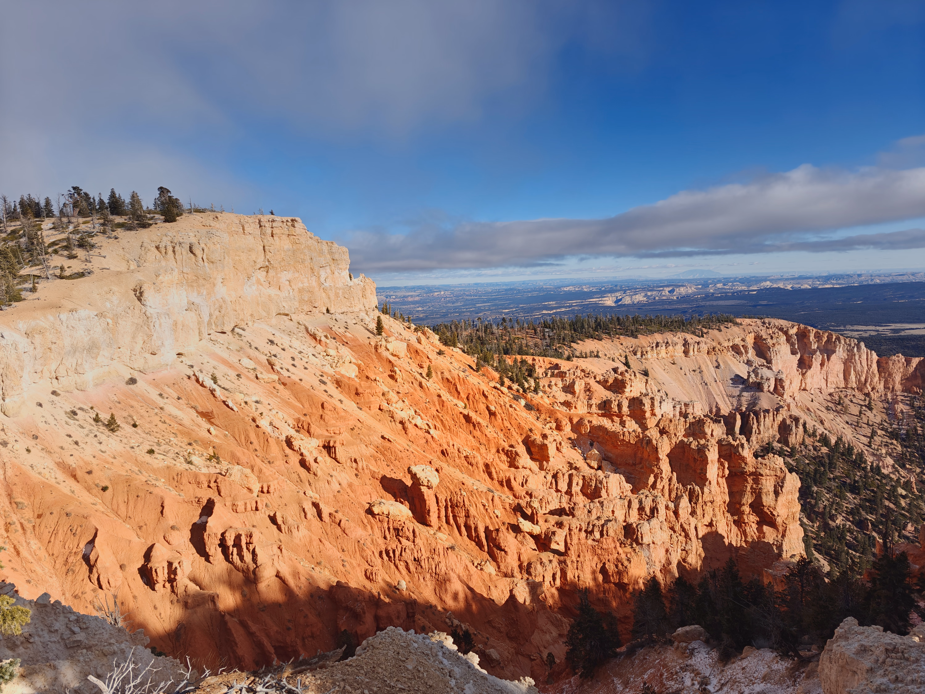 A bright band of sun crosses red Bryce Canyon walls while blue-gray storm cloud gathers above.