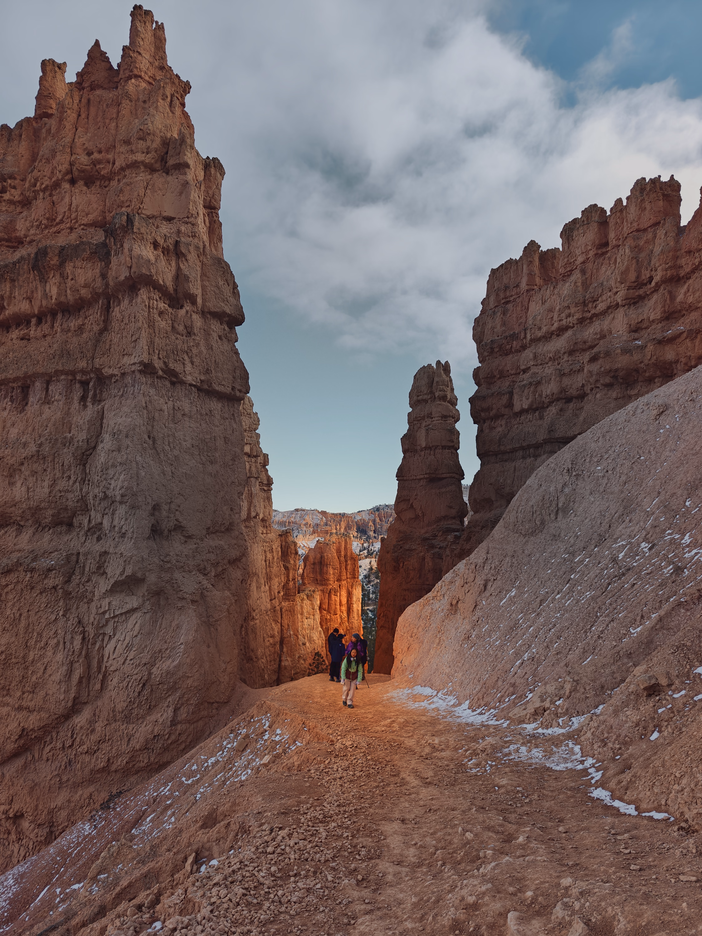 Hikers walk through a narrow corridor between tall orange hoodoos at Bryce Canyon.