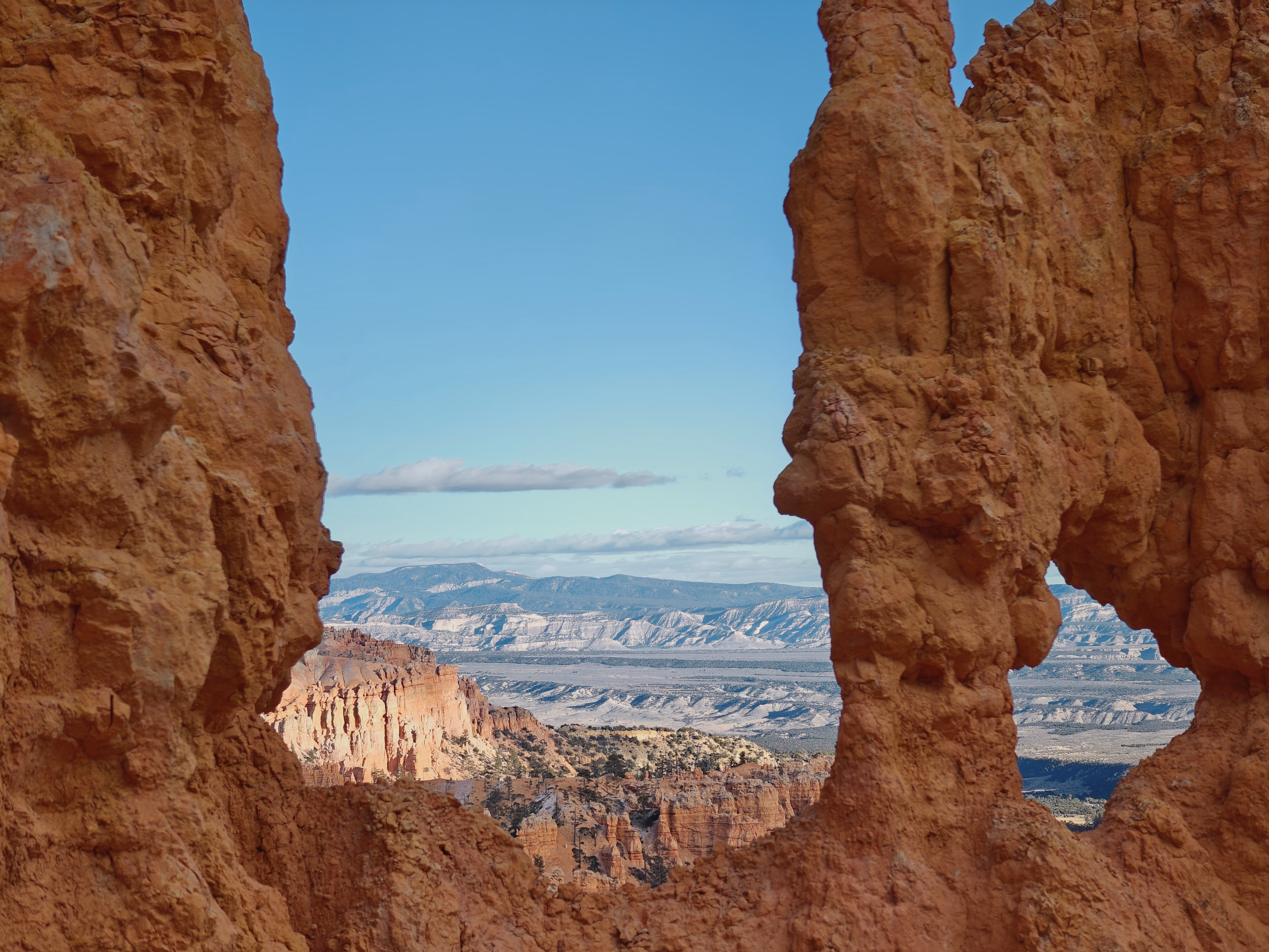 A natural arch and two orange rock pillars frame the pale desert beyond Bryce Canyon.