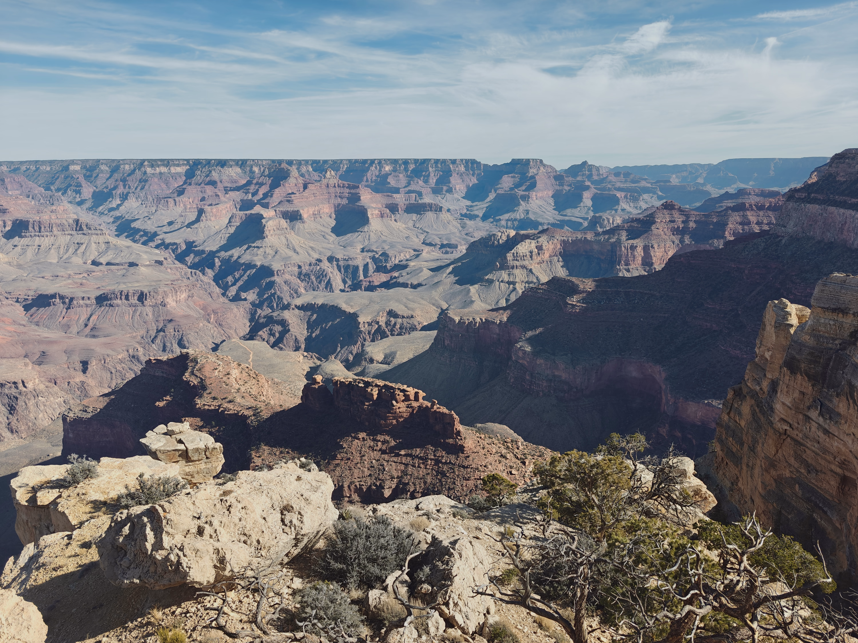 Sunlit foreground stone gives way to nested Grand Canyon ridges and cool-shadowed depth.