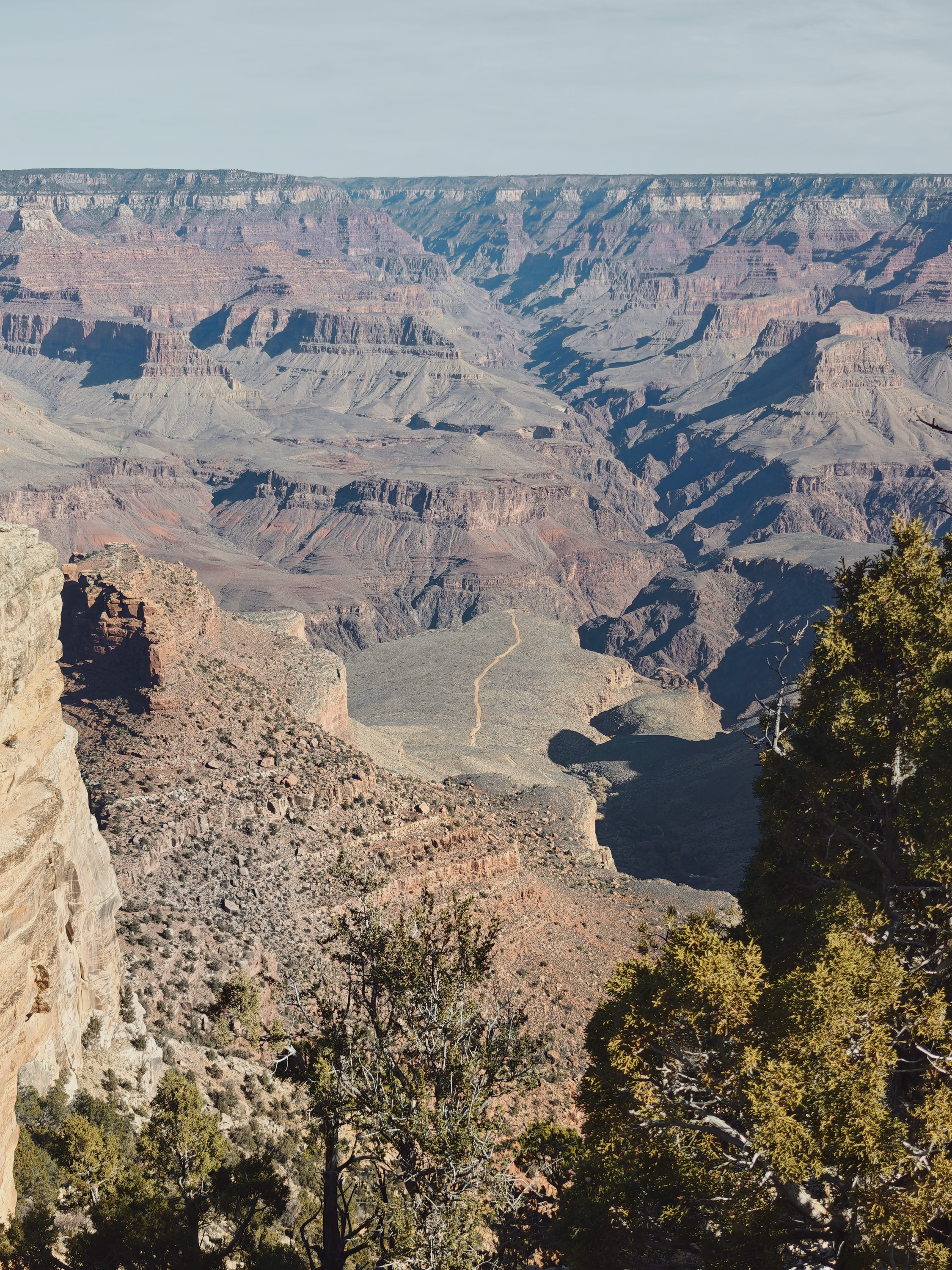 A high Grand Canyon view descends through terraces toward a distant pale road.