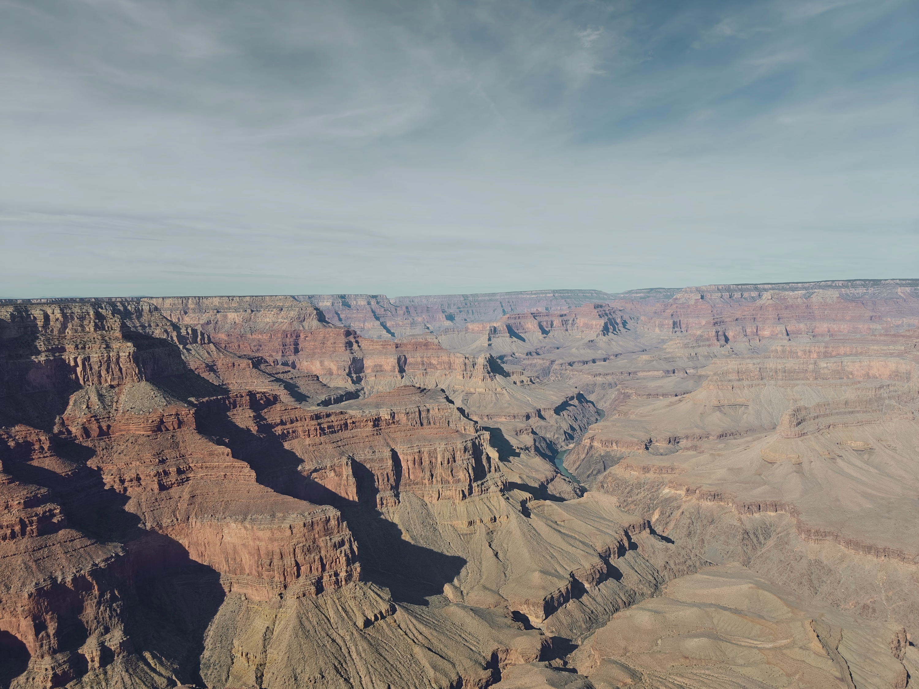 Sunlight divides layered Grand Canyon walls while the Colorado River bends far below.