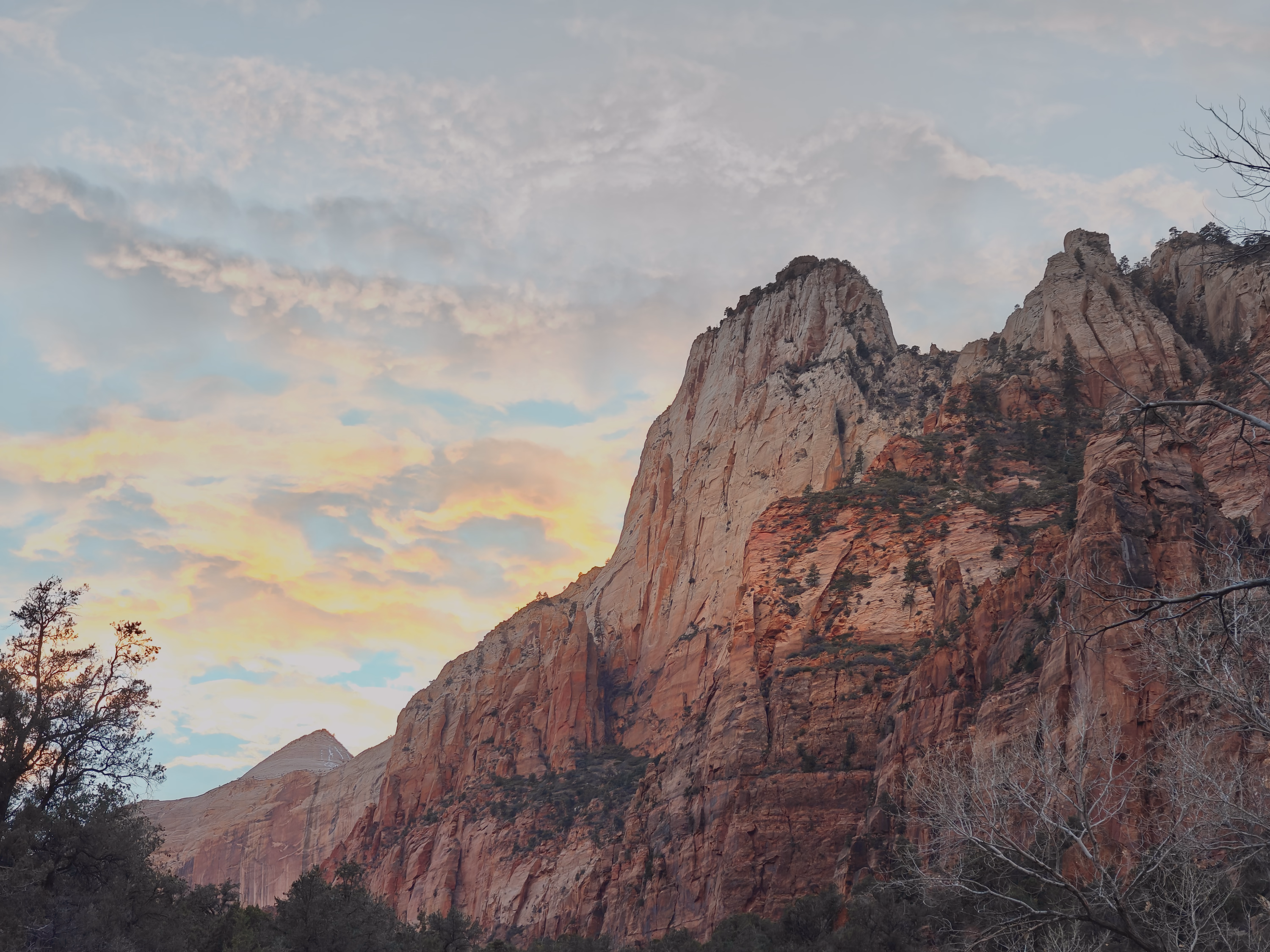 A wide red Zion cliff holds beneath peach-lit evening clouds and muted blue sky.