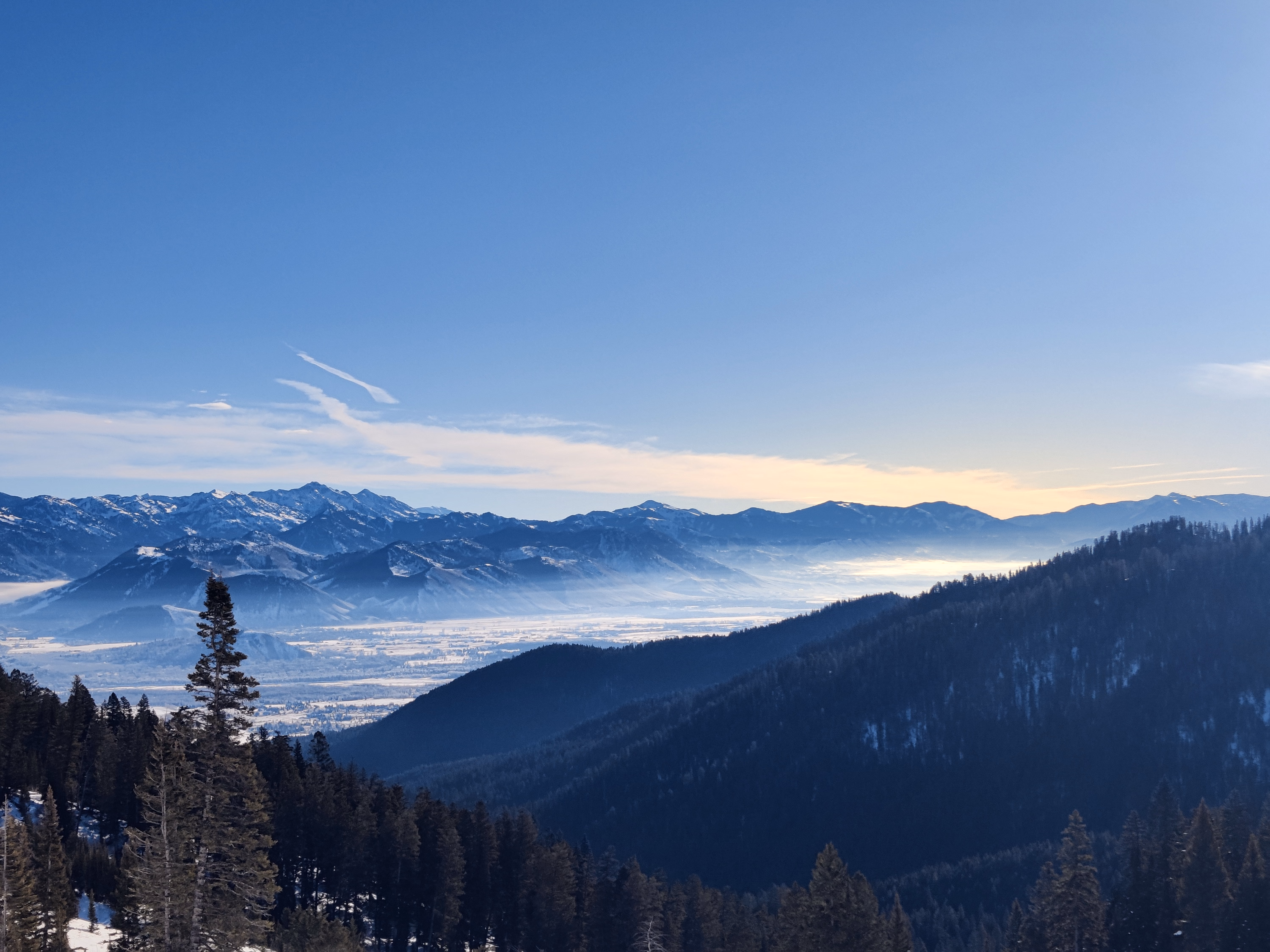A blue-hour Wyoming valley lies under low fog with a dark mountain ridge in the distance.