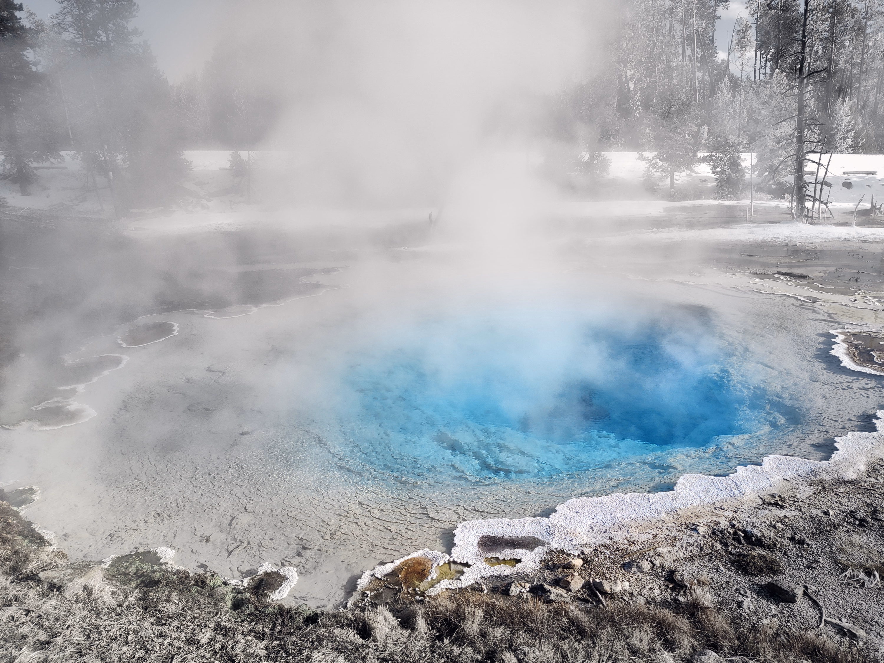 Blue geothermal water emerges through a veil of white steam inside a mineral basin.