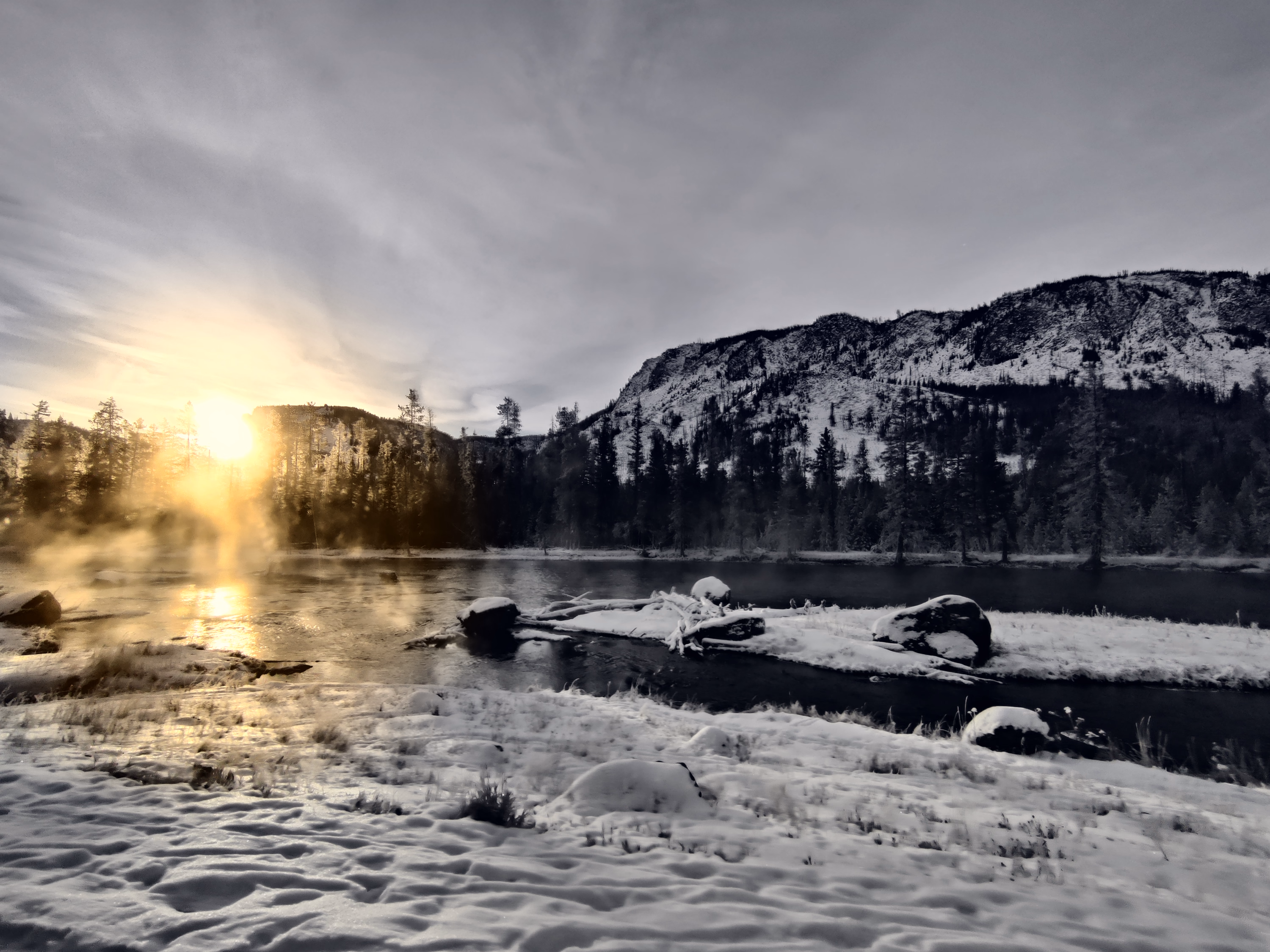 Low sun turns mist above the Yellowstone River gold while snow and a dark ridge hold the frame.